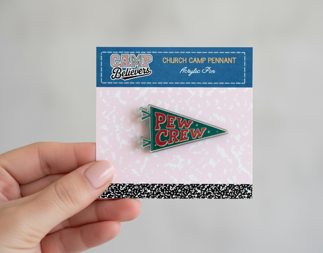 Pew Crew pennant pin on a card held by a hand against a gray background